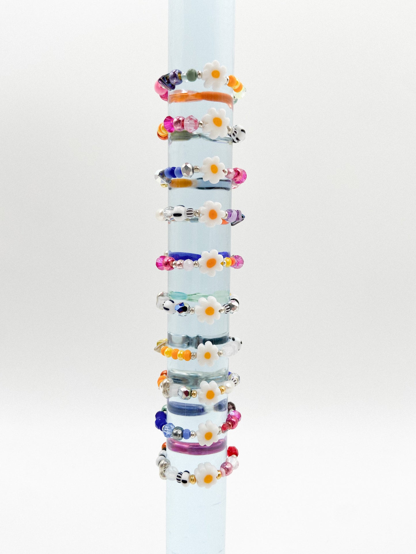Plexiglasstange auf der bunte Perlenringe mit zentraler Blume aufgereiht sind.